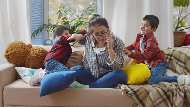 Exhausted woman sit on sofa feels irritated by loud hyperactive little children. Realtime