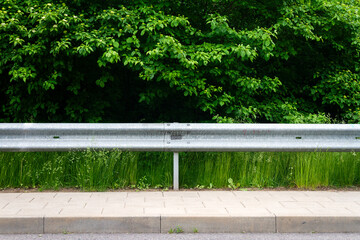 Sidewalk, highway guard rail, green grass and bushes
