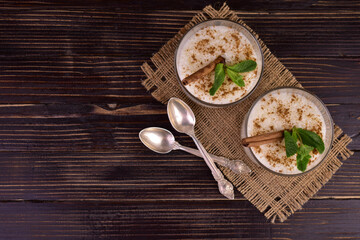 Rice pudding with cinnamon in glasses on a dark wooden background. Flat lay. Copy space.
