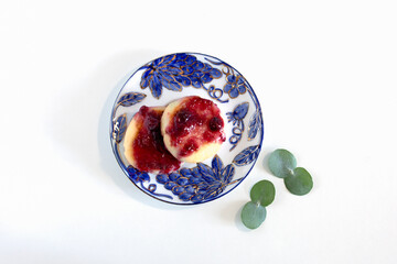 Cheesecakes with berry jam on a plate with a beautiful pattern stand on a white table. Photo of breakfast in a plate top view.