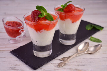 Rice pudding with strawberry jam in glasses on a white wooden background.
