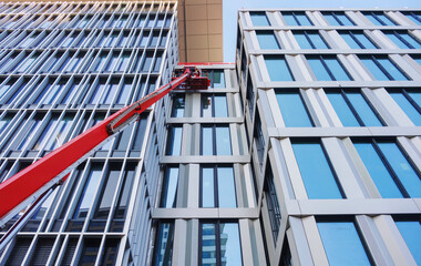 Construction worker using a cherry picker for mounting a Curtain wall facade of a contemporary...