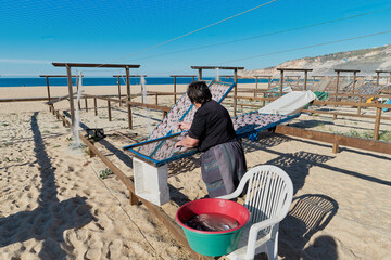 Portugese woman drying fish on the beach. Traditional portuguese food snacks