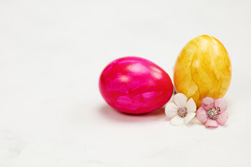 Easter eggs painted in pastel colors on a white background with copy space and cute spring flowers, Happy Easter Holiday concept with space for text. Yellow pink and blue