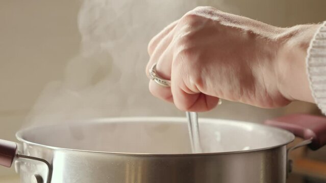 Closeup of young woman cooking soup stirring ingredients in hot water. Healthy nutrition, cooking at home, hot steam