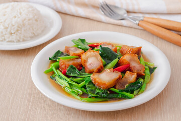 Stir fried kale with crispy pork in oyster sauce and rice on white plate