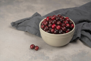 Cranberries with green leaves in small white bowl on the grey table. Fresh cranberries. Copy space. Selective focus. Macro. Closeup.