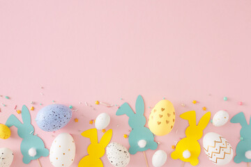 Easter decor concept. Top view photo of yellow blue white eggs easter bunny toppers and sprinkles on pastel pink background with copyspace. Holiday card idea