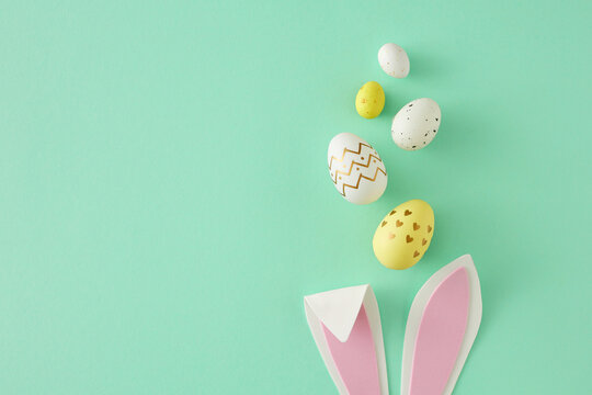 Naklejka Easter concept. Top view photo of easter bunny ears yellow white eggs on isolated teal background with copy space. Holiday card idea