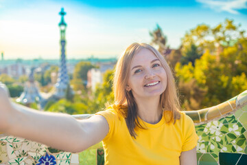 Beautiful young woman looking at camera taking photo with smart phone smiling in Park Guell,...