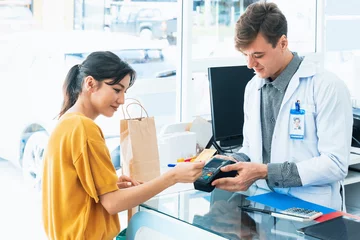 Fotobehang Payment by credit card with payment terminal in qualified drugstore. Modern financial payment of electric money. Satisfied customer purchase medication in pharmacy with prescription from pharmacist. © Summit Art Creations
