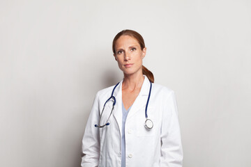 Serious friendly doctor or nurse with stethoscope wearing white lab coat uniform standing indoors