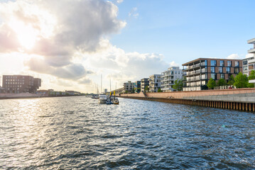 Modern apartment buildings in a redevelopped area along a former river harbour at sunset. Boats moored to a jetty are visible in the middle of the harbour. - obrazy, fototapety, plakaty