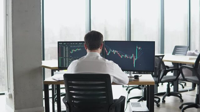 Back view of trader is working with multiple computer screens full of charts and data analysis and stock broker trading online. Concept of bitcoin and stock market trading