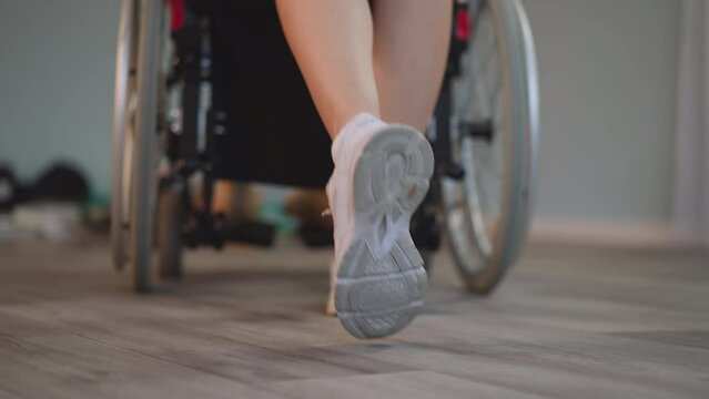 Legs of young woman pushing wheelchair with patient with disability on blurred background. Nurse takes care of person with paralysis at home closeup