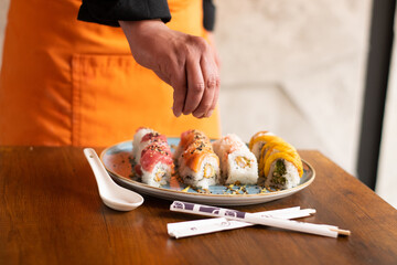 sushi on a plate. Hand of a man placing sesame seeds on sushi on his plate. Hands of a cook decorating the sushi plate with sesame seeds.