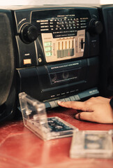 Finger pressing on 'Play' button on a 90s tape recorder with a loaded cassette tape