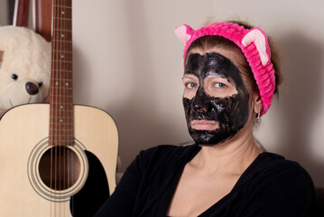 A middle-aged woman takes care of the skin of her face, sits and rests with a charcoal peel-off mask on face, skin care after 40 years. Concept of beauty and healthy skin