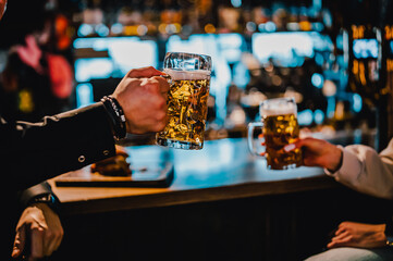 man and woman hands toasting with glasses of light beer at the pub or bar