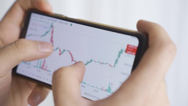 Close-up of man looking at stock market, stock, investment charts on phone.
Man Using Phone Displaying Real Time Stocks, Currency Market Charts.

