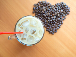 a cup of coffee with ice and a red straw next to a heart shaped pile of coffee beans, cookies on background.Top view