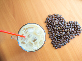 a cup of coffee with ice and a red straw next to a heart shaped pile of coffee beans, cookies on background.Top view