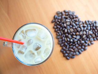 a cup of coffee with ice and a red straw next to a heart shaped pile of coffee beans, cookies on background.Top view