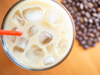 Ice coffee on a wood table with ice and red straw, coffe beans on background. Cold summer drink with red tube.Above close-up view flatlay