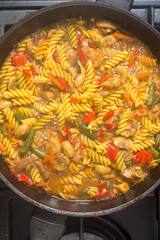 Pasta with vegetables and mushrooms in sauce and spices in a frying pan close-up.
