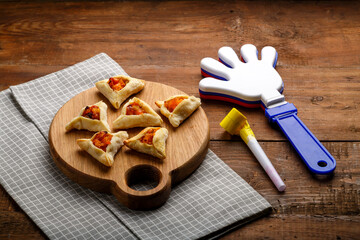 cookies triangles gometashi mishloach manot for Purim laid out on a wooden board on a napkin next to clappers and a whistle.