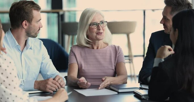 Good looking mature business lady in glasses leads group formal meeting with staff members. Professional corporate coaching, share knowledge to younger employees. Negotiations with company partners