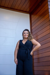 fat woman empowered in front of a house, successful businesswoman with hand on waist wearing elegant black jumpsuit, person in front of a house