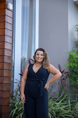 fat woman empowered in front of a house, successful businesswoman with hand on waist wearing elegant black jumpsuit, person in front of a house