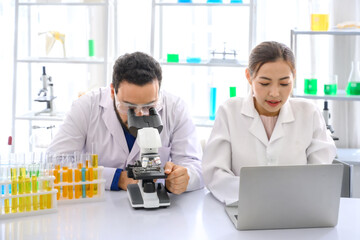 A male scientist is using a microscope to look and do some research. with a female assistant...
