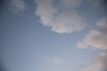crescent moon in the evening sky by clouds soft lighting during dawn