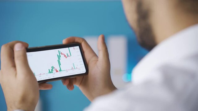 Male hands holding phone checking stock market chart for trading and investing in crypto exchange.