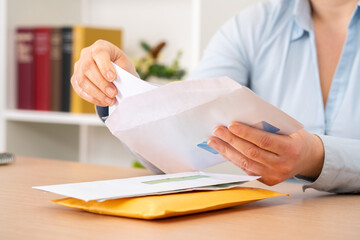 Close up of woman hands putting a letter inside an envelope on a desk at home or office - obrazy, fototapety, plakaty