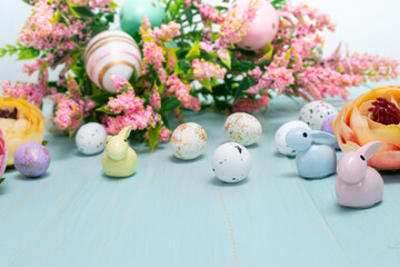Easter composition of pink spring flowers, colorful roses, cute bunnies and decorative eggs. Advertising content for Easter holiday on blue wooden background. Flat lay, side view, close up, copy space