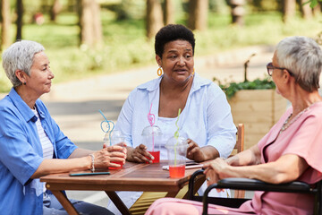 Diverse group of senior women enjoying drinks at outdoor cafe and chatting