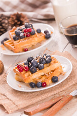 Waffles with red currant and blueberries on white dish.