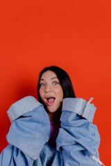 Close-up portrait of charming joyful beautiful girl posing with jeans against a bright red background. People emotions, lifestyle leisure, creative fashion concept.