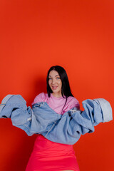 Close-up portrait of charming joyful beautiful girl posing with jeans against a bright red background. People emotions, lifestyle leisure, creative fashion concept.