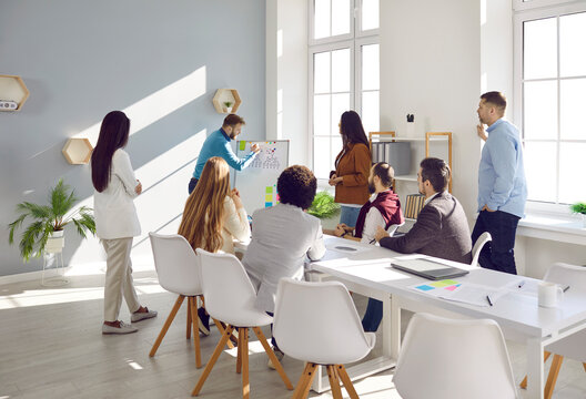 Business man makes presentation and explains strategy on board in front of colleagues. Business people in brainstorm in office talking, solving current issues and discussing project. Business concept.