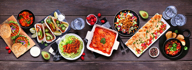 Healthy plant based vegetarian meal table scene. Above view on a dark wood banner background....