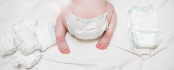 A baby in a diaper crawls on a white sheet next to dirty and clean diapers. A huge number of...