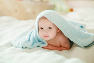 A funny little girl peeks out from under a blue towel in the children's room. The child after hygienic procedures is happy.