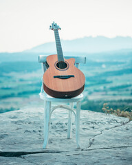 Guitarra acústica sobre una silla. Música en la naturaleza. Puesta del sol con montaña de fondo.