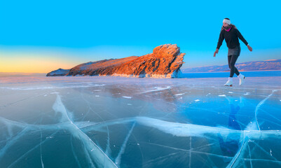 A young happy woman is skating on the transparent ice of the frozen Lake Baikal on a sunny winter...