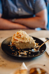 Coconut cream pie, on black plate with spoon on wooden table with companion sitting across table
