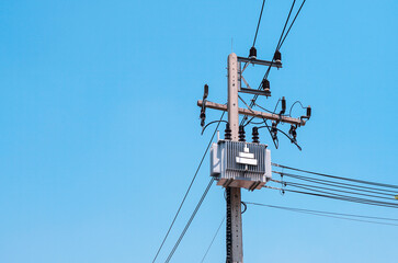 AC high-voltage power transformer on electric pole with wires on a background of blue sky, high...